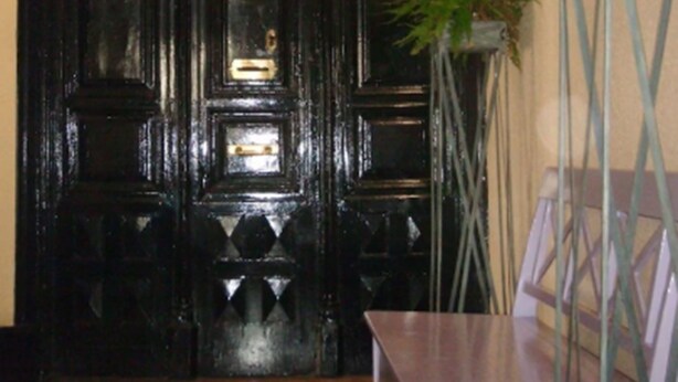 A dark wooden door with intricate designs, a potted plant, and a small table in a room with wooden flooring. - Puerta del Sol Rooms (Madrid)