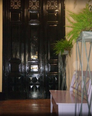 A dark wooden door with intricate designs, a potted plant, and a small table in a room with wooden flooring. - Puerta del Sol Rooms (Madrid)
