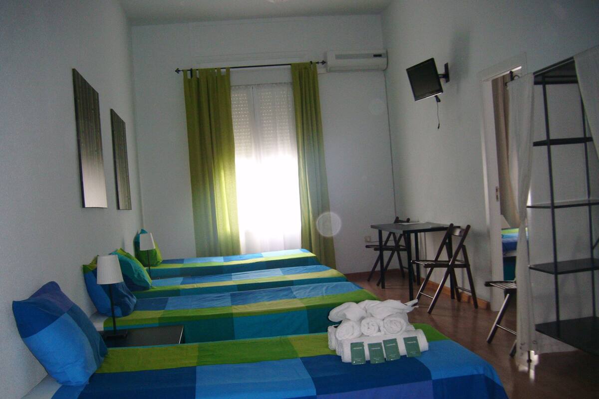 A hotel room with two beds, a desk, a chair, a TV, and a window with curtains.