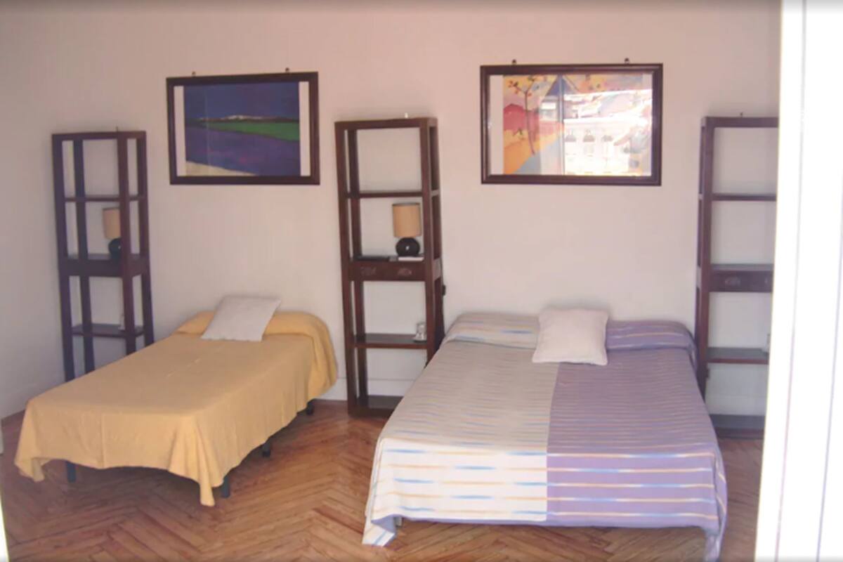 A room with two single beds, wooden furniture, and two framed pictures on the wall.