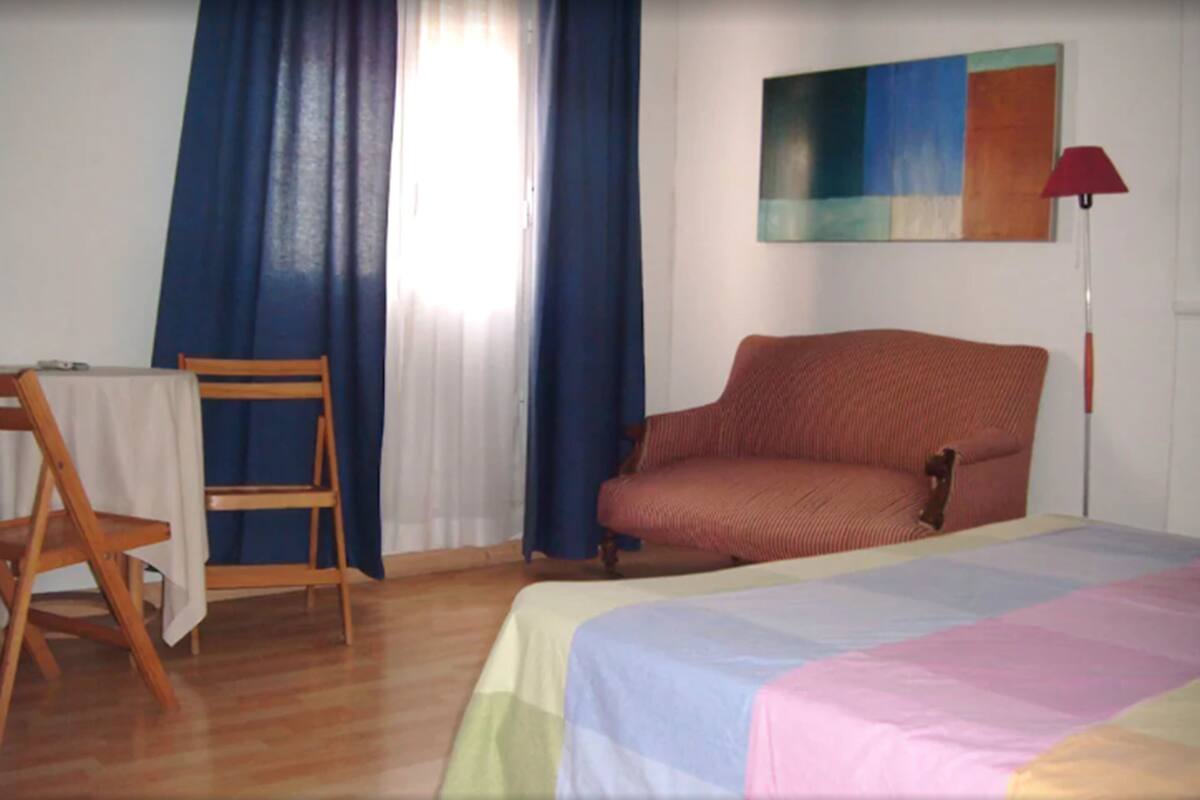 A room with a bed, a chair, a desk, and a painting on the wall.