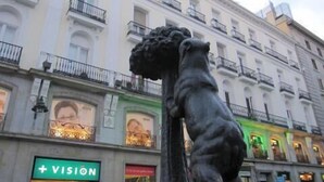 A statue in front of a building with balconies and a sign that reads "+VISION". - Puerta del Sol Rooms (Madrid)