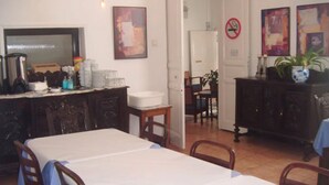 A dining area with a long table, chairs, a coffee station, and a door leading to another room. - Puerta del Sol Rooms (Madrid)