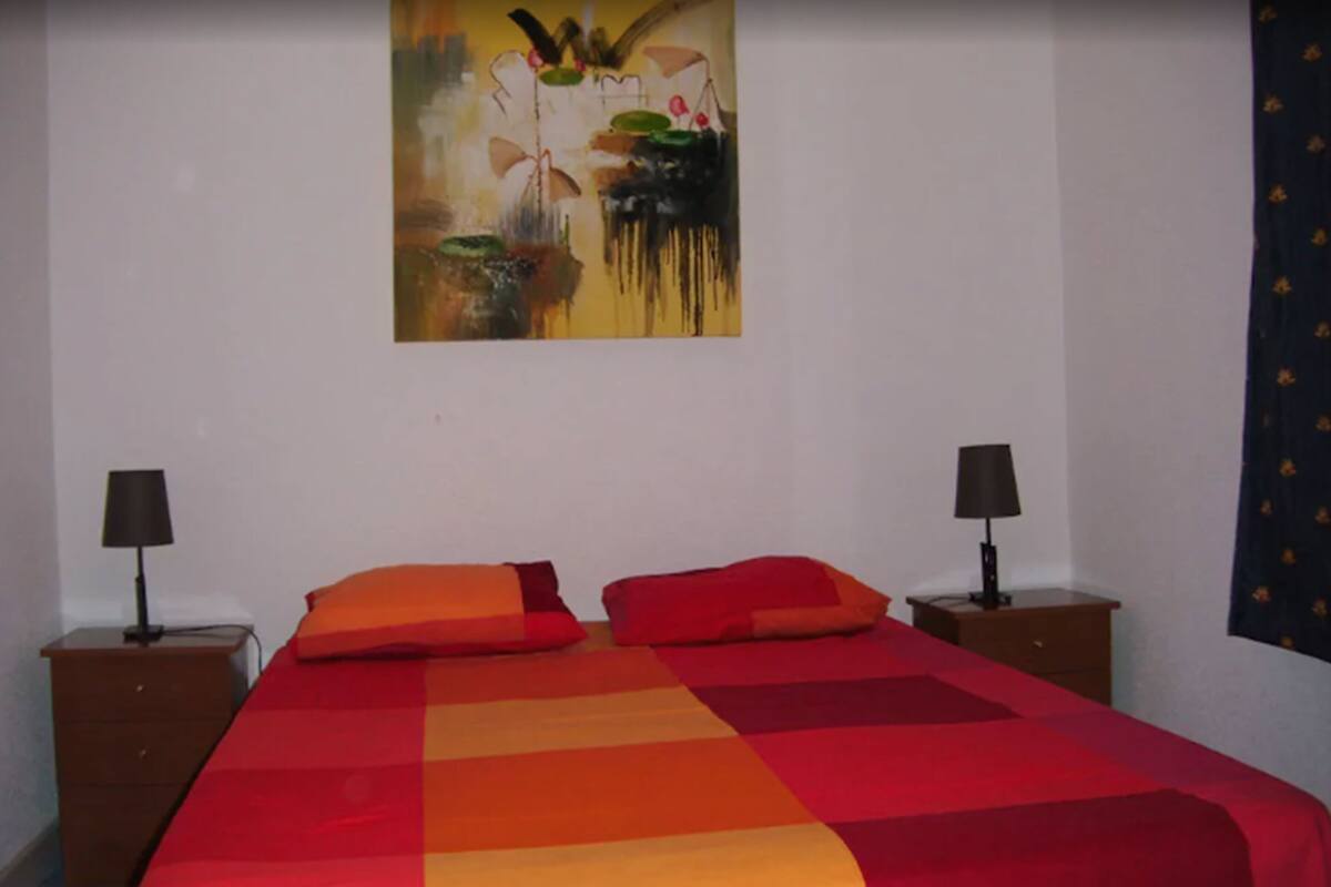 A bedroom with a bed, two nightstands, and a painting on the wall.