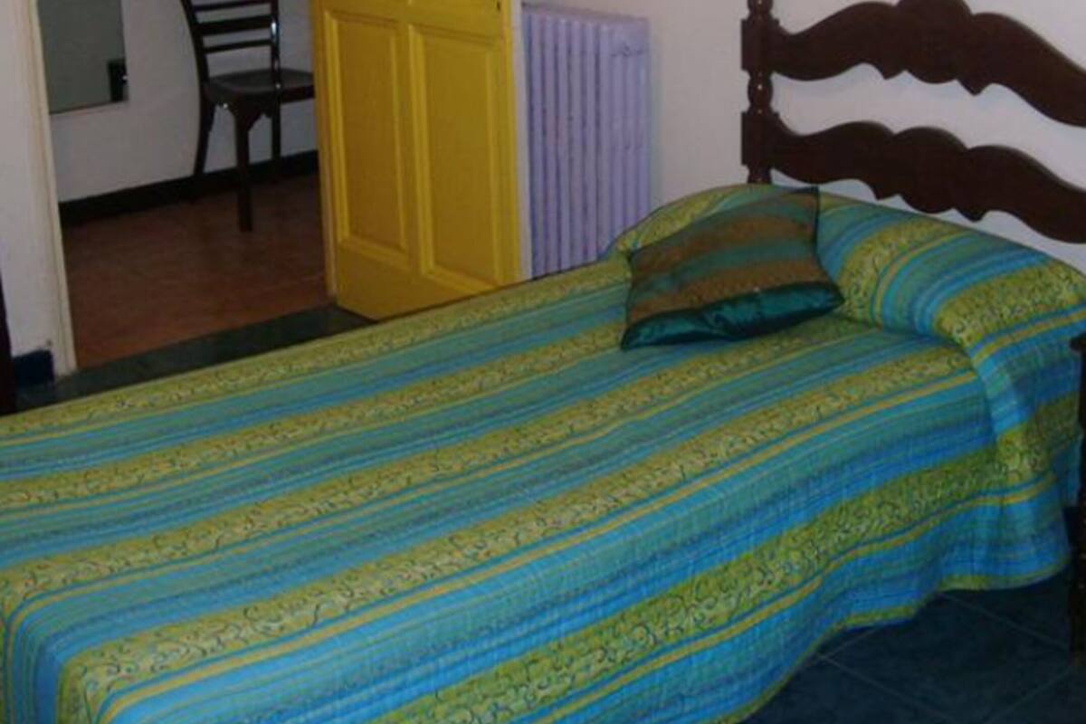 A bedroom with a bed, a chair, a radiator, and a door.