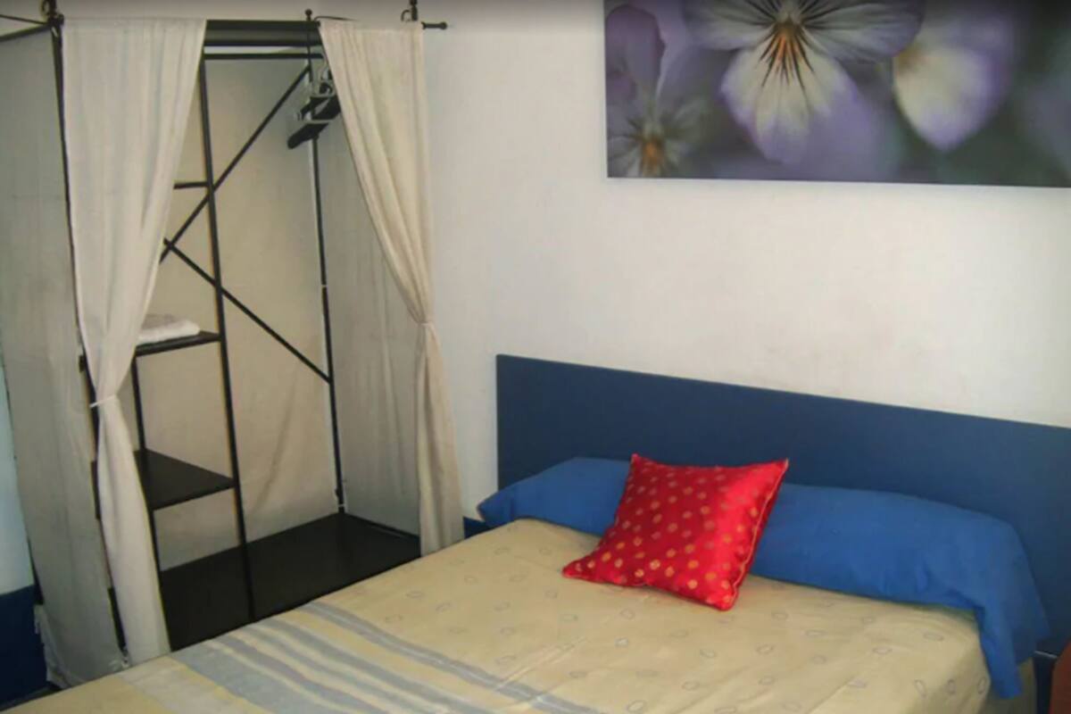 A single bed with a blue headboard and a red pillow, a white canopy, and a wall-mounted shelf.