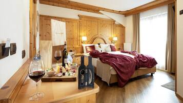 A hotel room with a wooden headboard, a bed with a red blanket, a wooden desk with a wine glass, a bottle of wine, and a bottle opener.