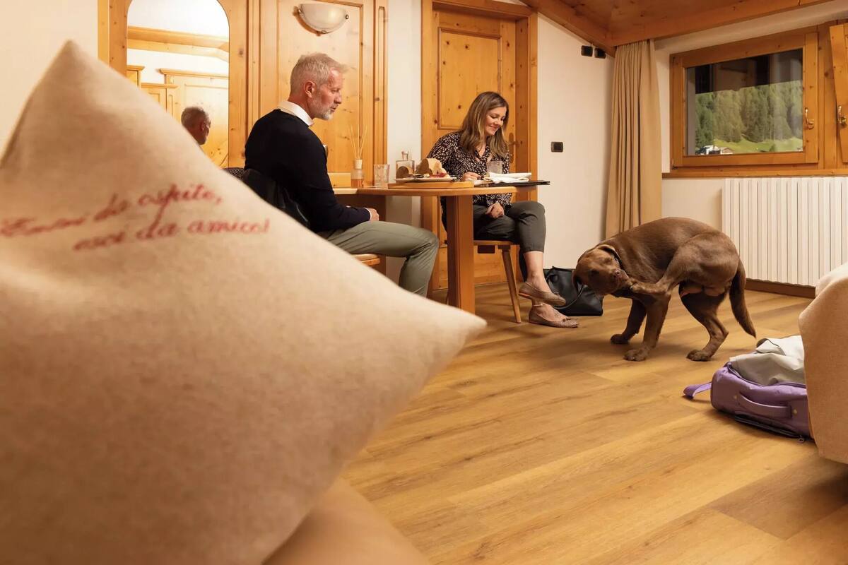 A wooden interior with a dining table, two people seated, and a dog on the floor.