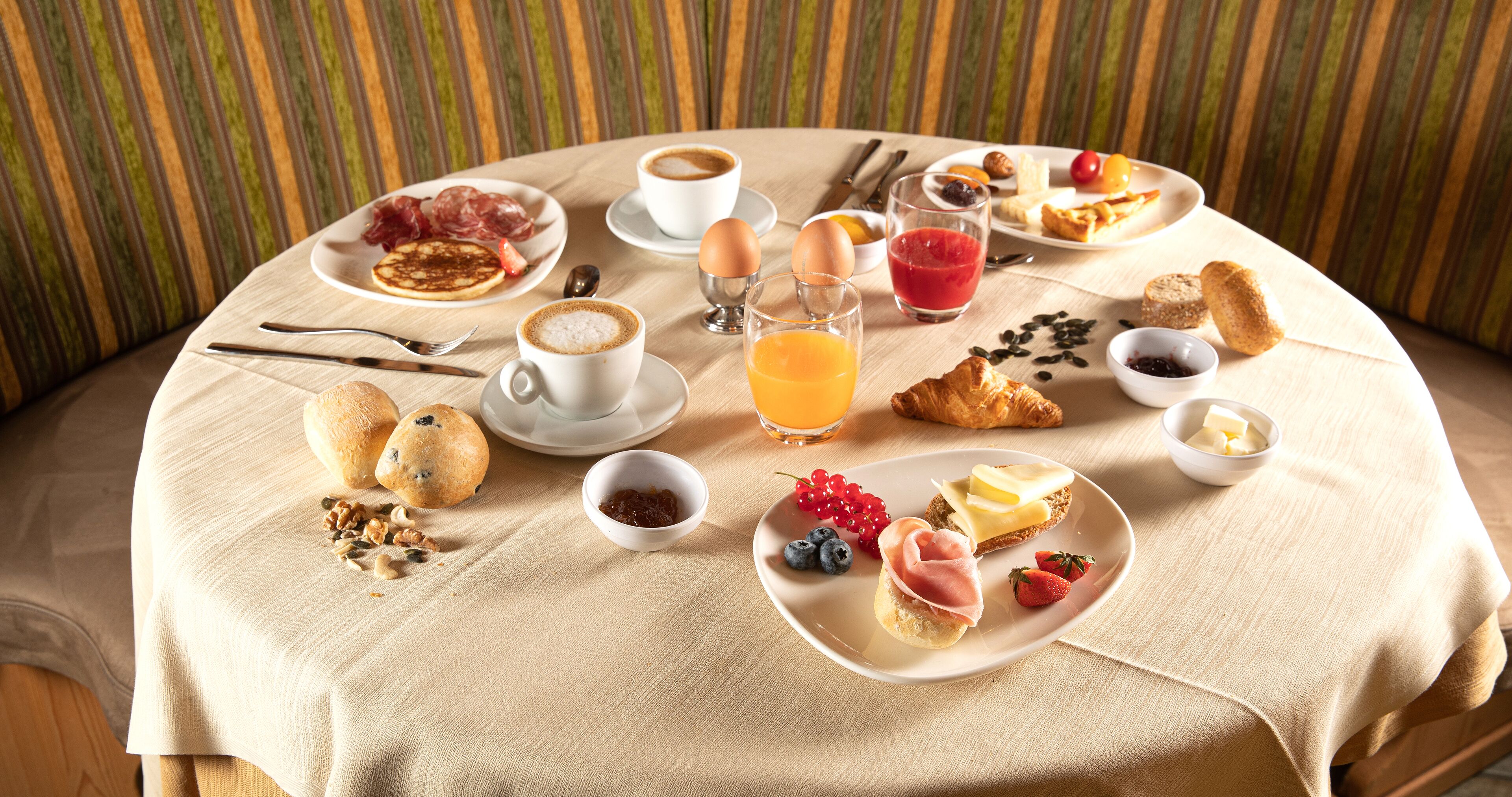 Una mesa de desayuno con diversos alimentos, tazas de café y un vaso de zumo de naranja.