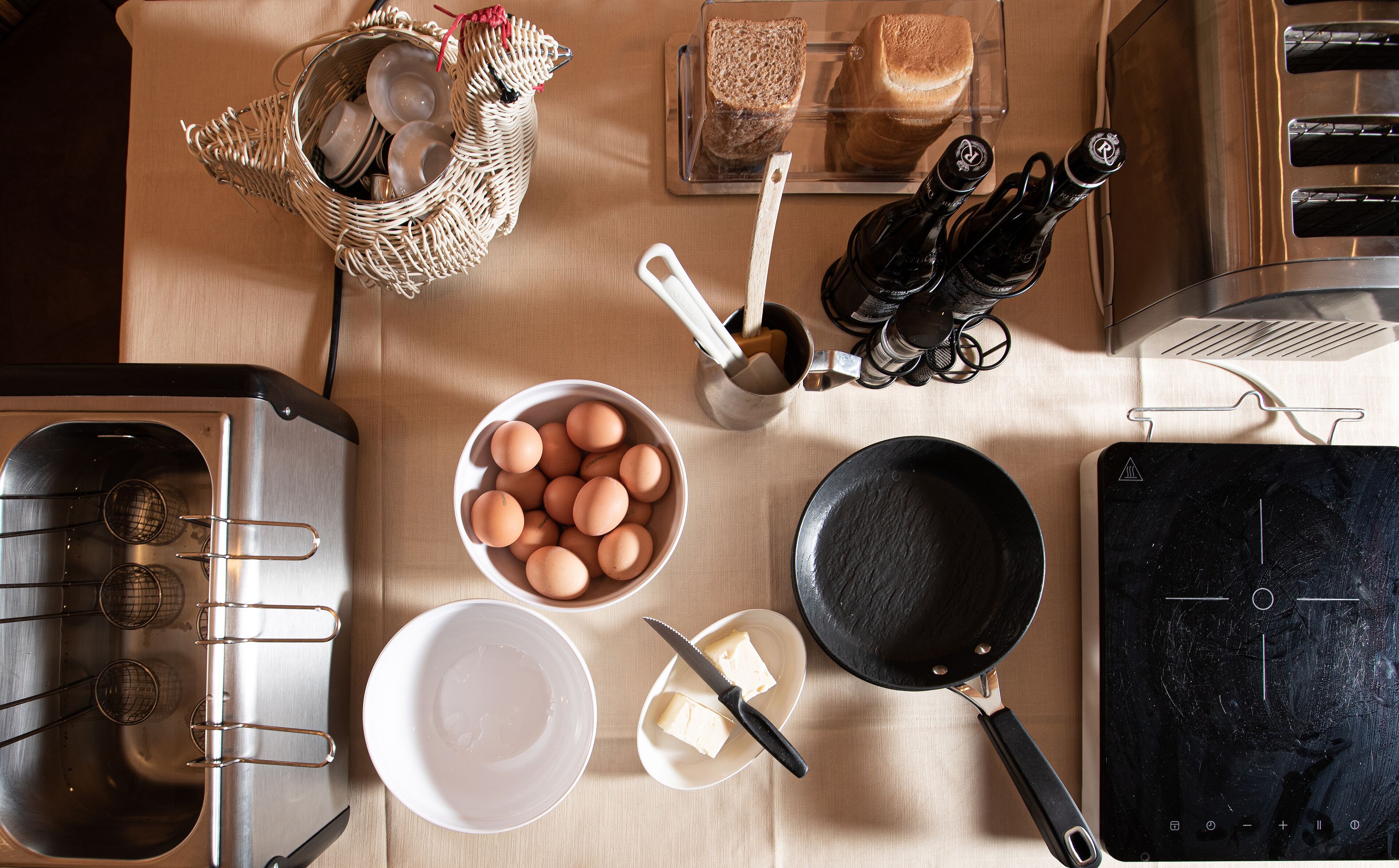 A kitchen with a sink, stove, frying pan, eggs, butter, bread, and salt and pepper shakers.