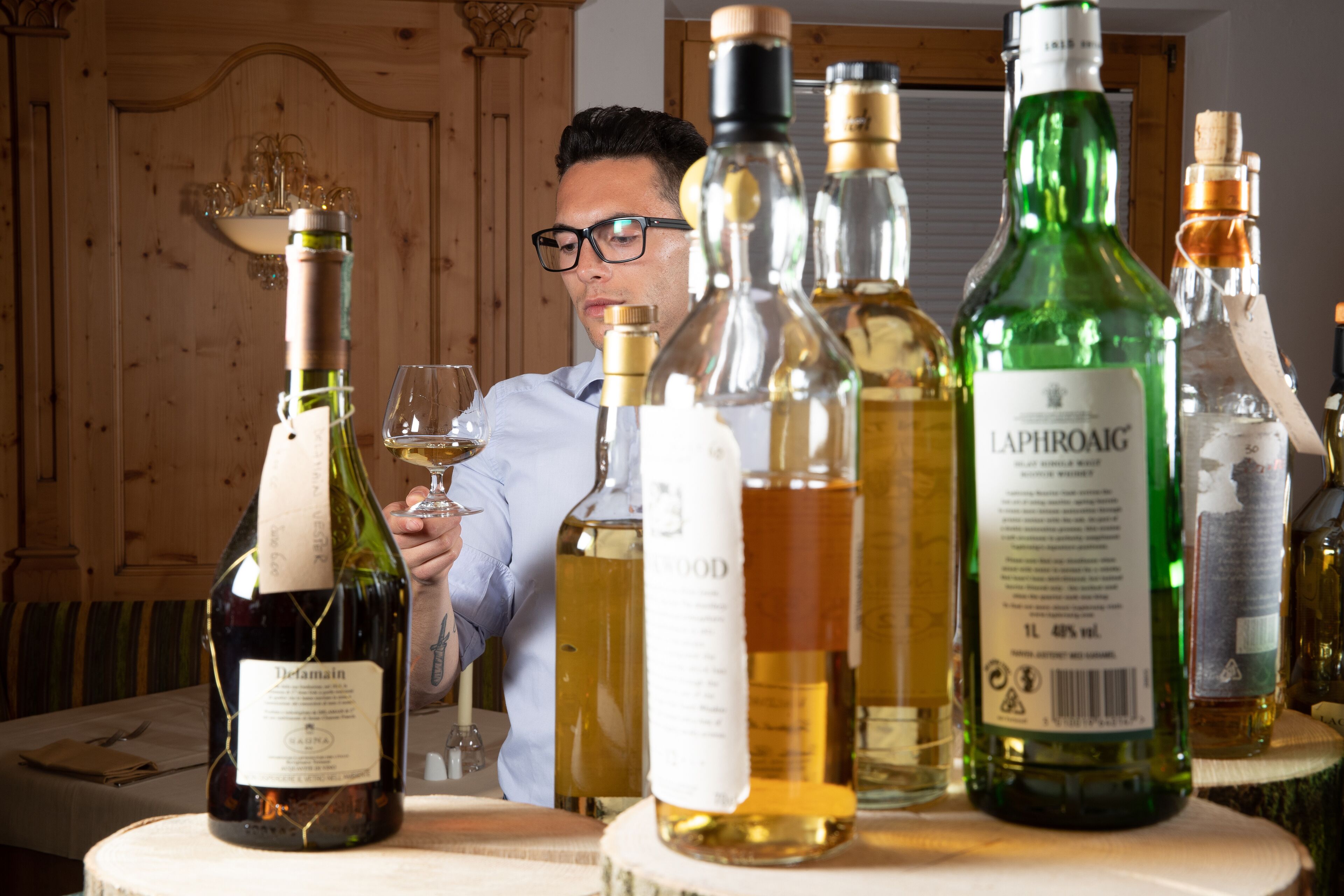 A table with various bottles of alcohol and a person holding a glass.