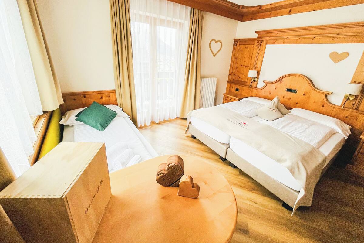 A hotel room with two beds, wooden headboards, a round wooden table, and a window with curtains.