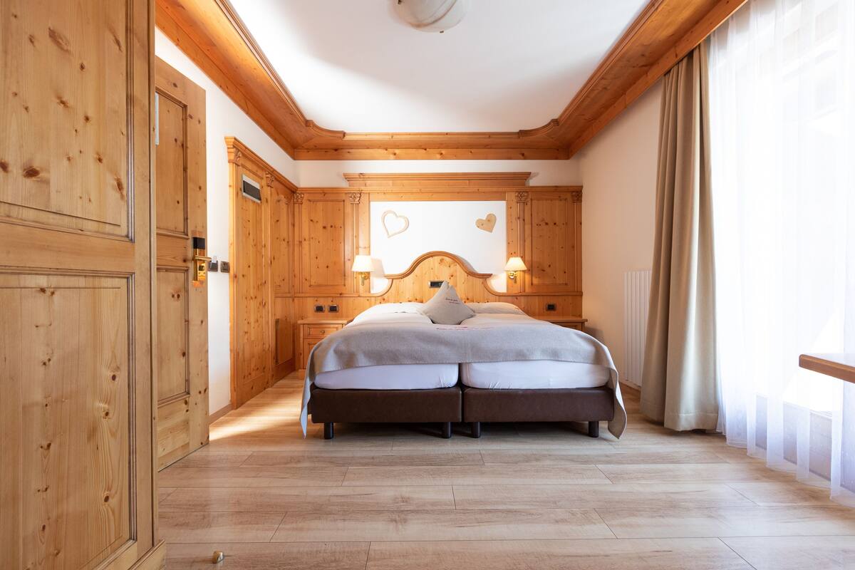 A bedroom with a double bed, wooden paneling, two bedside lamps, and a heart-shaped decoration on the wall.