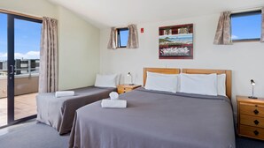 A hotel room with two beds, a large window, a painting, and a view of the sky.