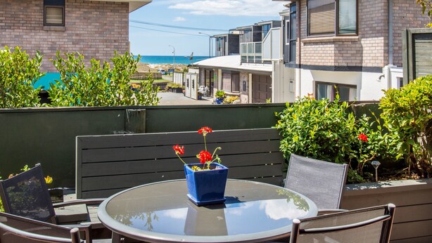 A patio with a glass table, chairs, and a blue flower pot.