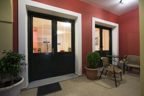 A hotel entrance with two black doors, a potted plant, and wicker chairs. - Hotel Irida (Lefkada)