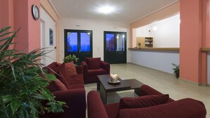 Sala de estar com sofás vermelhos, uma mesa de centro e uma planta. Duas portas dão acesso a outros cômodos.