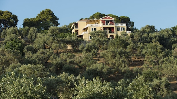 Uma casa de dois andares com uma varanda no andar superior, cercada por oliveiras.