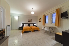A hotel room with two beds, a desk, a TV, and a kitchenette. - Hotel Irida (Lefkada)