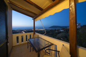 Uma varanda com mesa e cadeiras de vidro, com vista para a paisagem urbana e colinas.