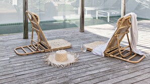 A wooden deck with two wicker lounge chairs and a small table, overlooking a pool area with tropical plants. - Cape Beach House (Byron Bay)