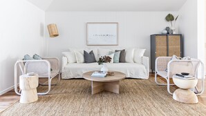 A modern living room with a white sofa, two wicker chairs, a round coffee table, and a rattan cabinet. - Cape Beach House (Byron Bay)