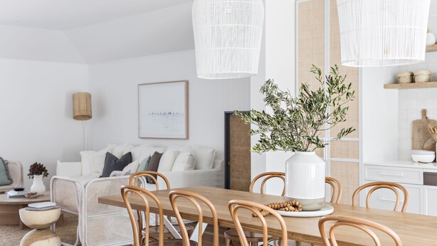 A modern dining area with a wooden table and chairs, white pendant lights, and a potted plant. - Cape Beach House (Byron Bay)