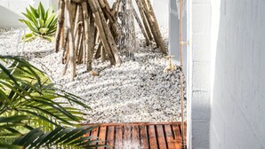 A treehouse shower with a white wall and a metal frame, surrounded by white pebbles and greenery. - Cape Beach House (Byron Bay)