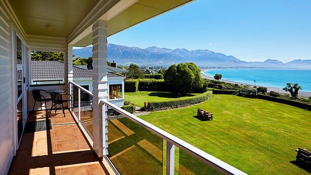 Un balcon offrant une vue sur une pelouse parfaitement entretenue, un espace patio aménagé avec du mobilier d’extérieur et, au loin, une chaîne de montagnes.