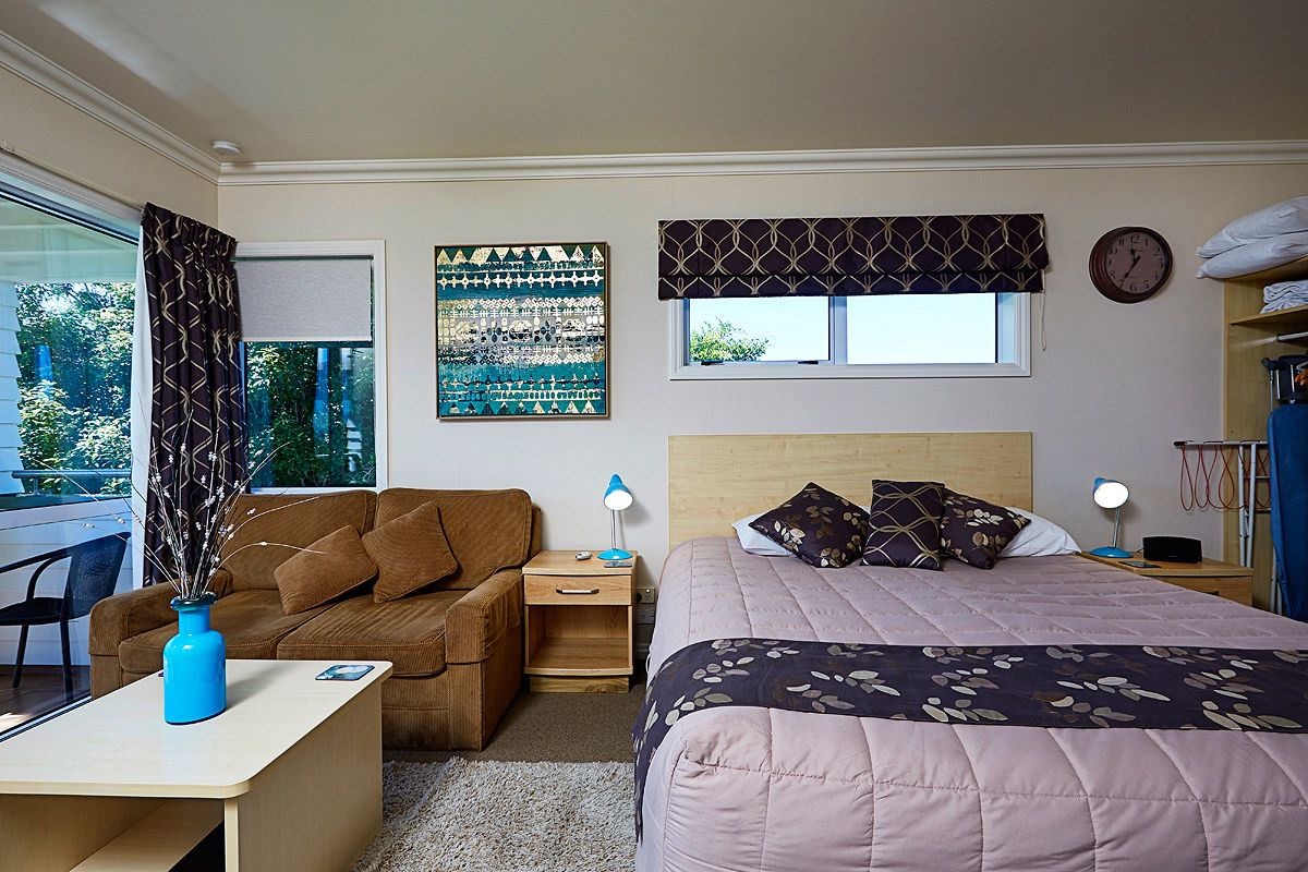 Un dormitorio con cama, escritorio, silla, ventana con cortinas, un reloj de pared y una estantería con toallas.