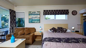 Un dormitorio con cama, escritorio, silla, ventana con cortinas, un reloj de pared y una estantería con toallas.