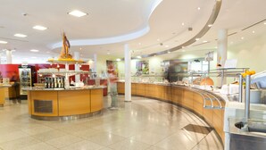 A modern, well-lit food court with a central island counter, glass display cases, and a variety of food options. - Akademiehotel Dresden (Dresden)