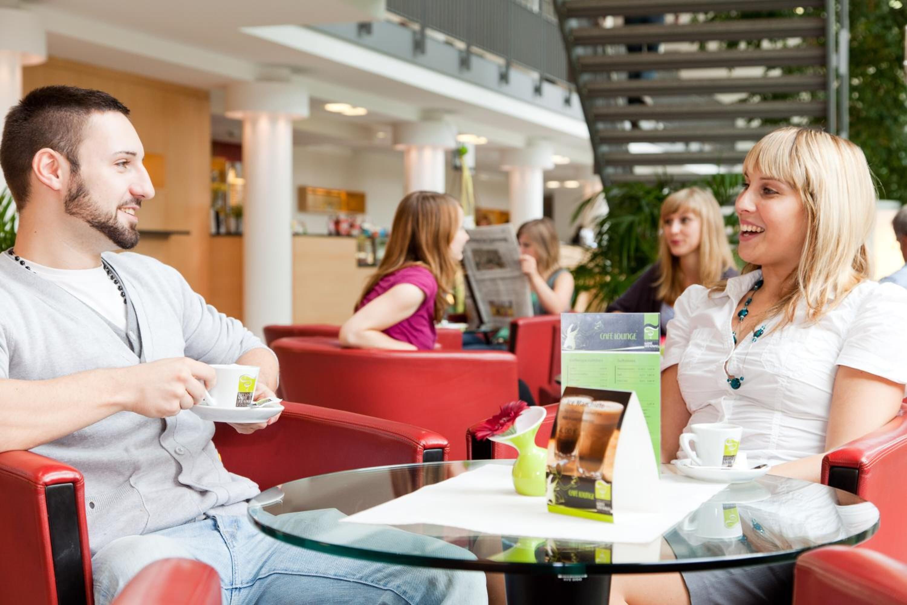 Et moderne opholdsområde indendørs med glasborde og røde stole.