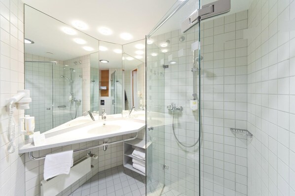 A modern bathroom with a glass-enclosed shower, a large mirror, and a white sink.