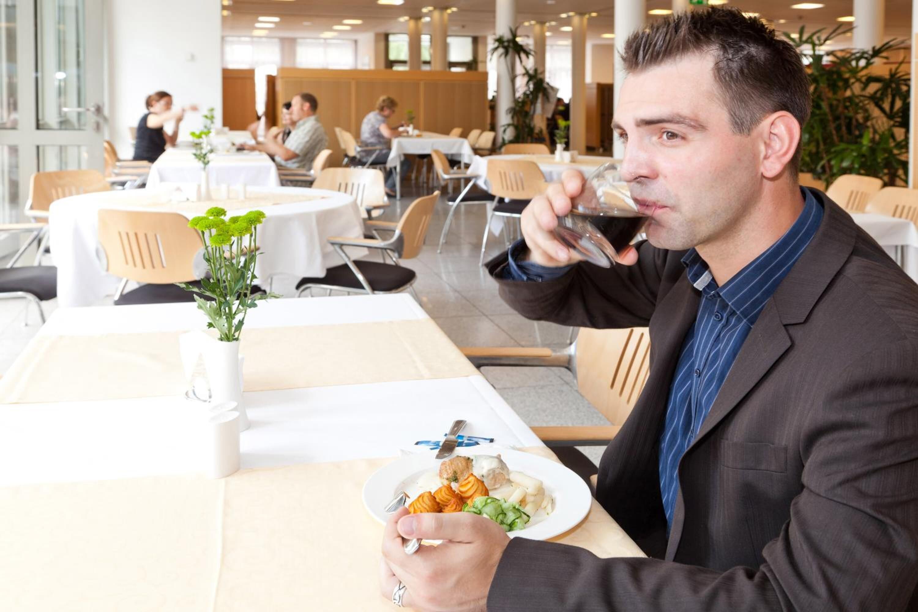 Un hombre cenando en un restaurante moderno con manteles blancos, sillas de madera y plantas en macetas.