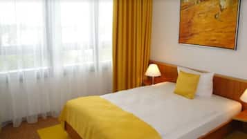 Una camera d'albergo con un letto, un comodino, una lampada, un quadro appeso al muro e una finestra con tende.