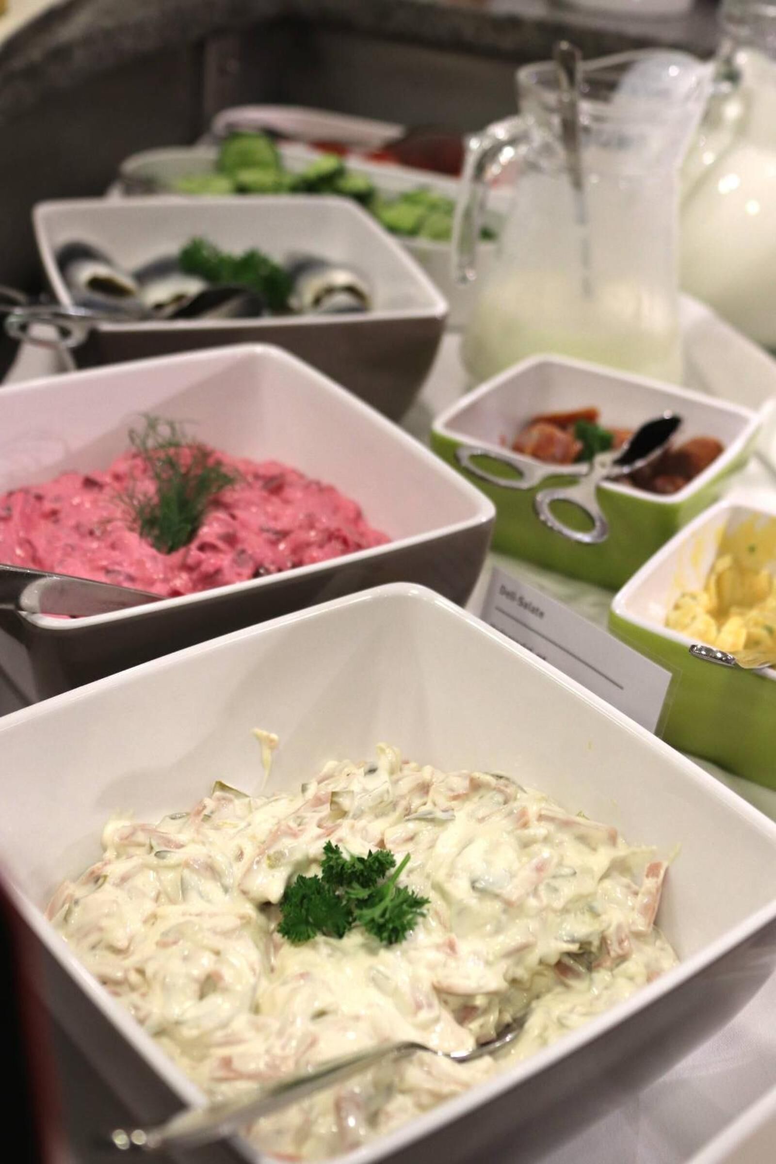 Un buffet proposant divers plats, notamment une salade crémeuse, une tartinade rose et un récipient vert contenant une fourchette.