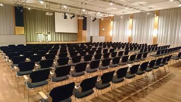 Een vergaderzaal met rijen stoelen, een podium en een groot scherm.