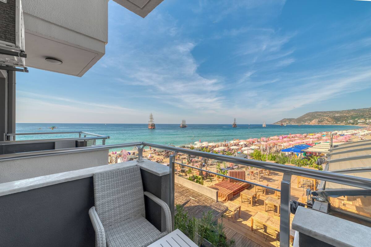 Un balcón con mobiliario de mimbre que da a una playa con sombrillas y vistas al mar.