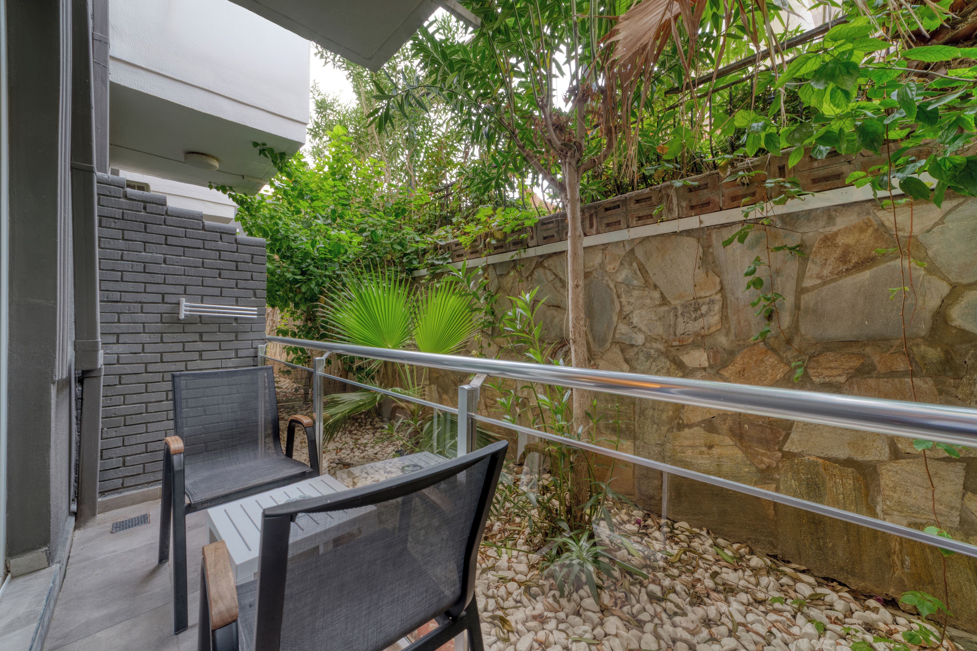 An outdoor patio area with a stone wall, a metal railing, and a seating arrangement.