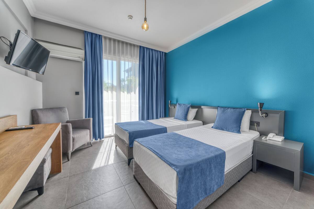 Habitación de hotel con dos camas, un escritorio, una silla, un televisor y una mesita de noche con teléfono.