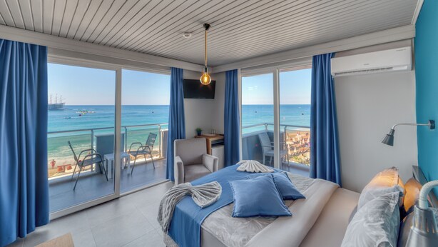 Quarto de hotel moderno com uma cama grande, uma mesa de trabalho e uma varanda com vista para o mar.