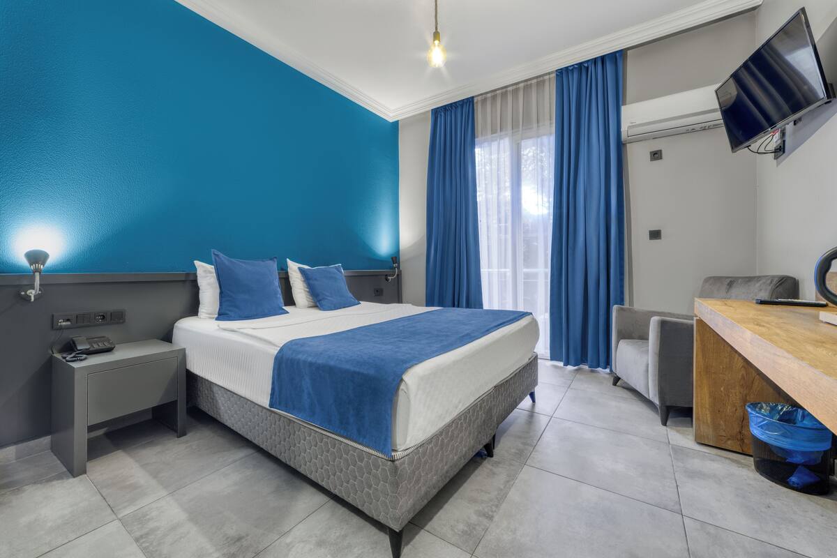 Una habitación de hotel moderna con cama, mesita de noche, escritorio y televisor.