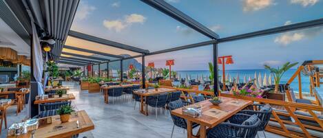 An outdoor dining area with tables and chairs, potted plants, and umbrellas.