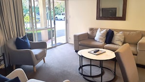 A living room with a sofa, armchairs, a coffee table, and a sliding glass door leading outside. - Tuscana Motor Lodge (Christchurch)