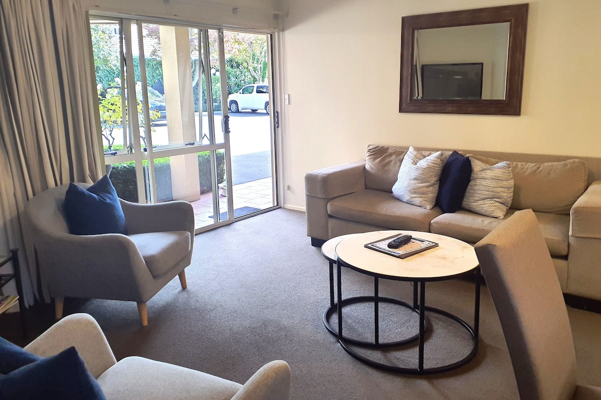A living room with a sofa, armchairs, a coffee table, and a sliding glass door leading outside.