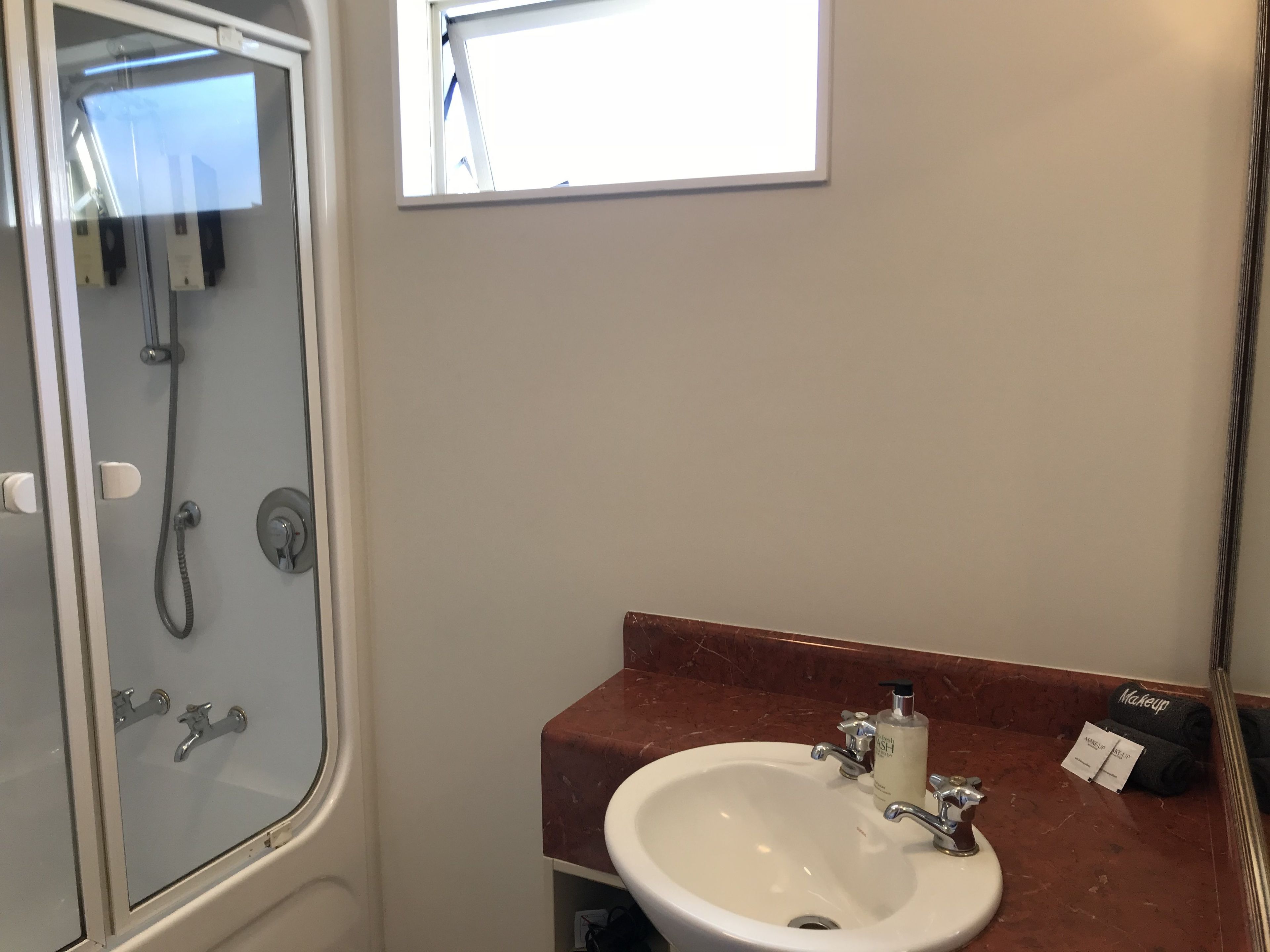 Un bany amb dutxa envidriada, un lavabo blanc amb taulell de marbre i un mirall que reflecteix l'espai.