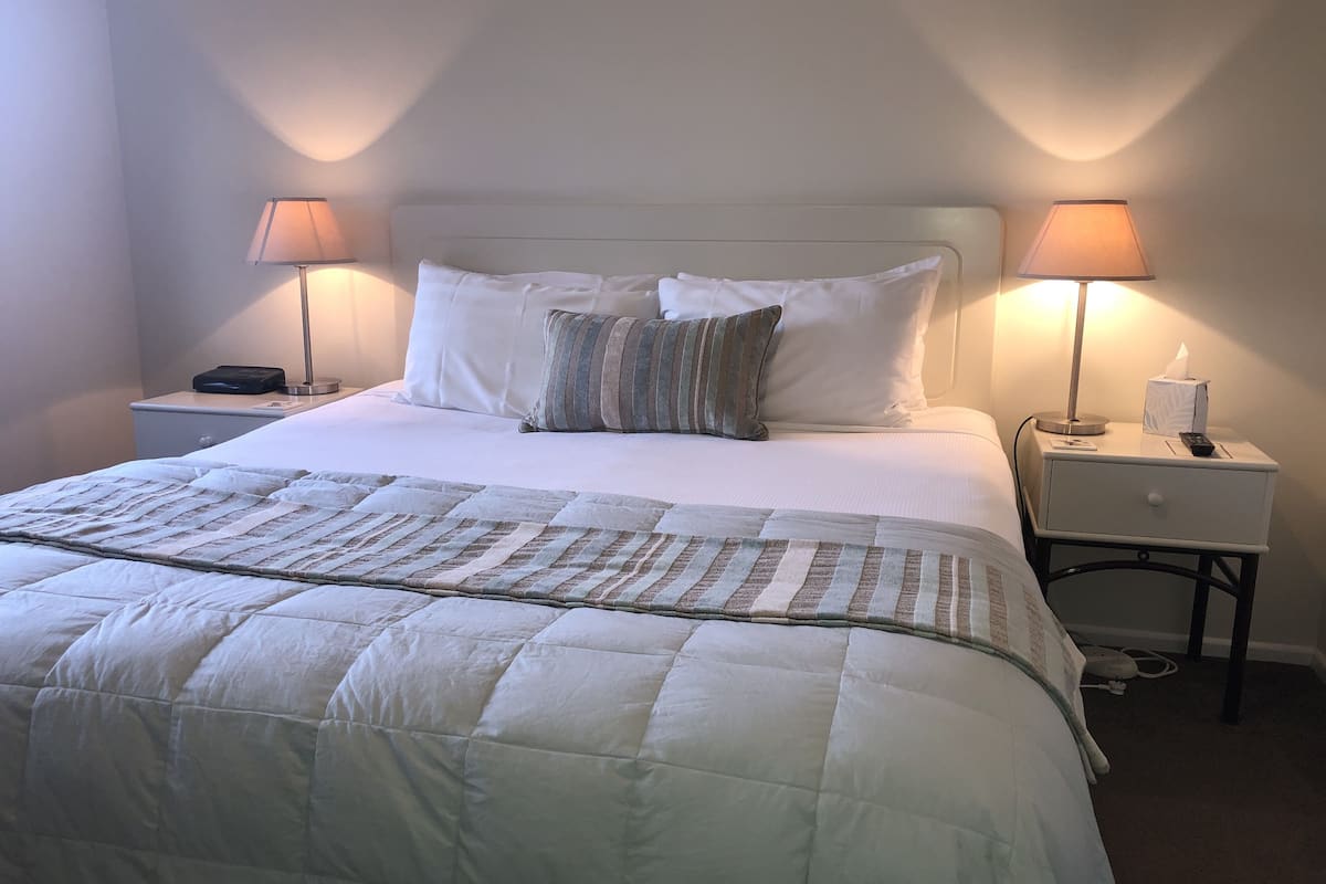 A neatly made bed with a white comforter and striped pillows, flanked by two bedside tables with lamps and a tissue box.