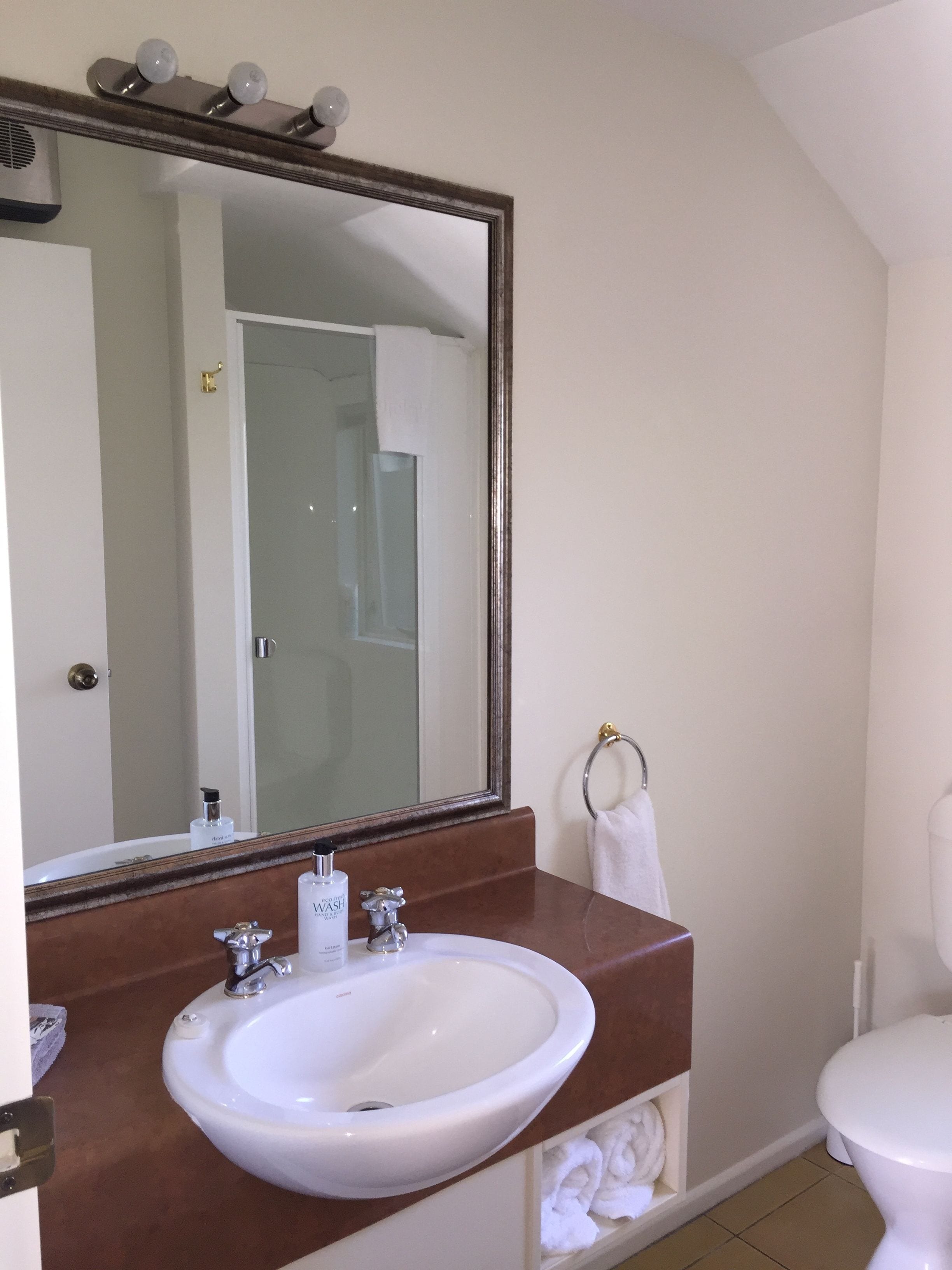 Un baño con un lavamanos blanco, un espejo grande y un inodoro.