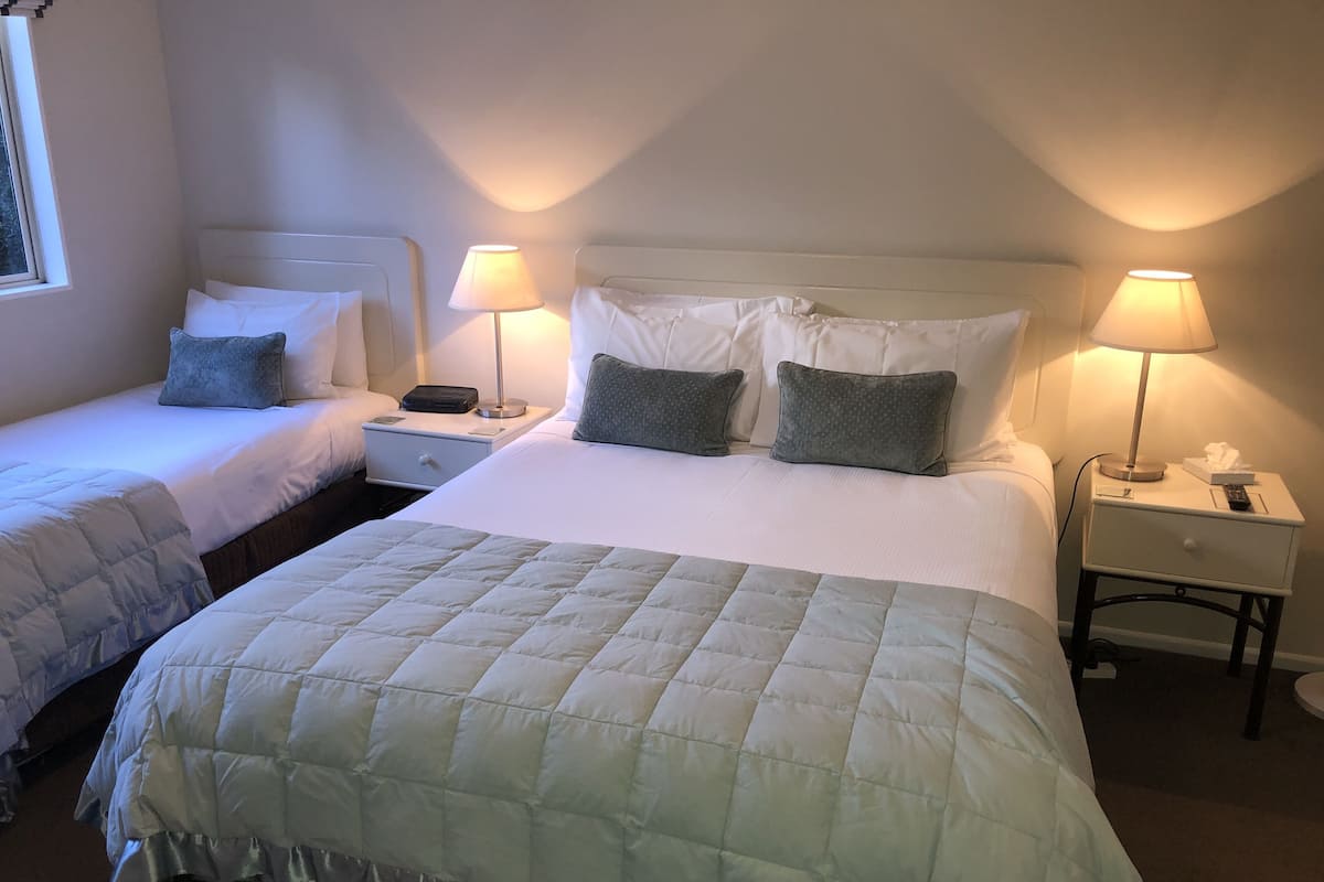 A hotel room with two single beds, each with a pillow and a bedside table with a lamp.